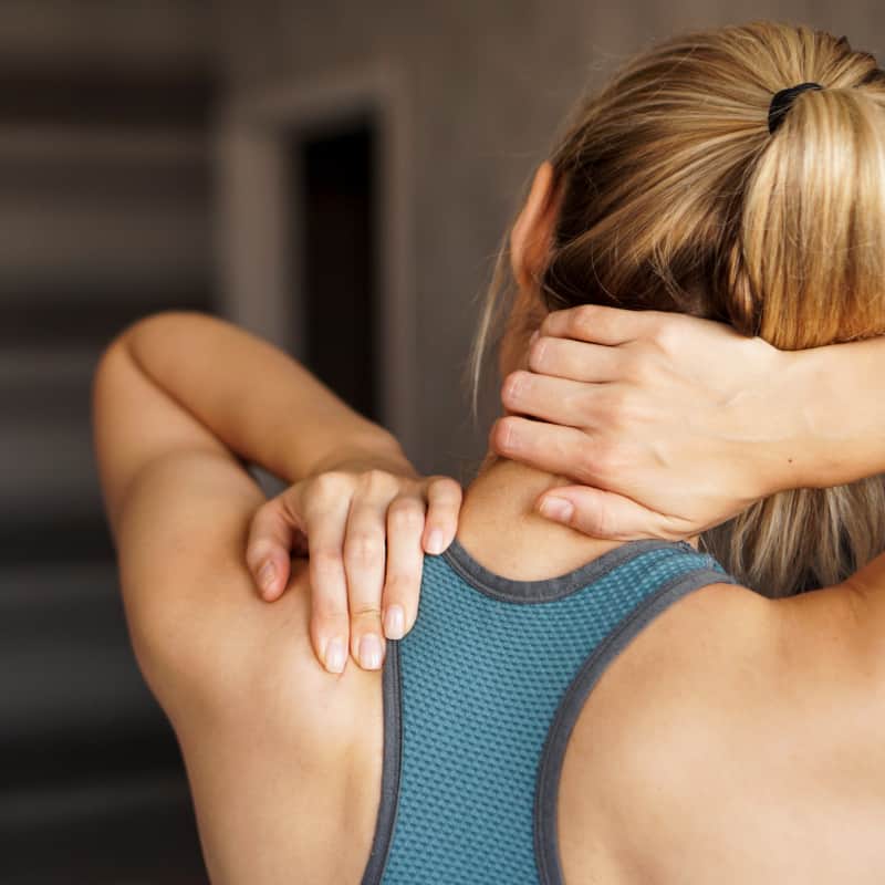 A image from behind a female grabbing her shoulder and neck in attempt to ease discomfort