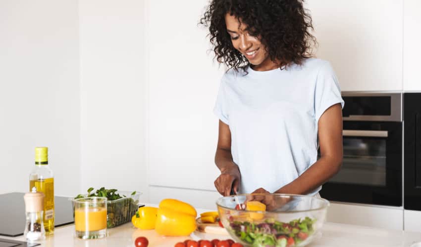 Young black woman smiling while preparing healthy meal of fruits and vegetables