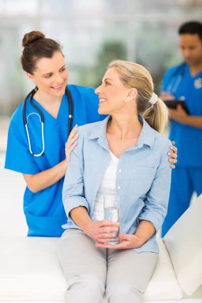 A middle aged woman being comforted by a female nurse, both smiling at each other.