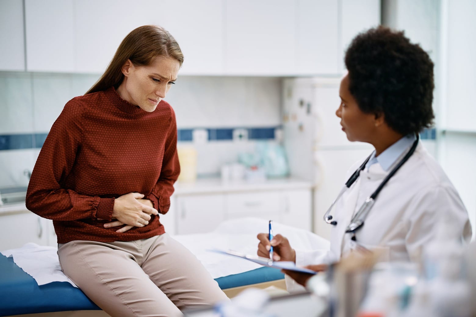 Mid adult woman with abdominal pain having medical appointment at doctor's office.